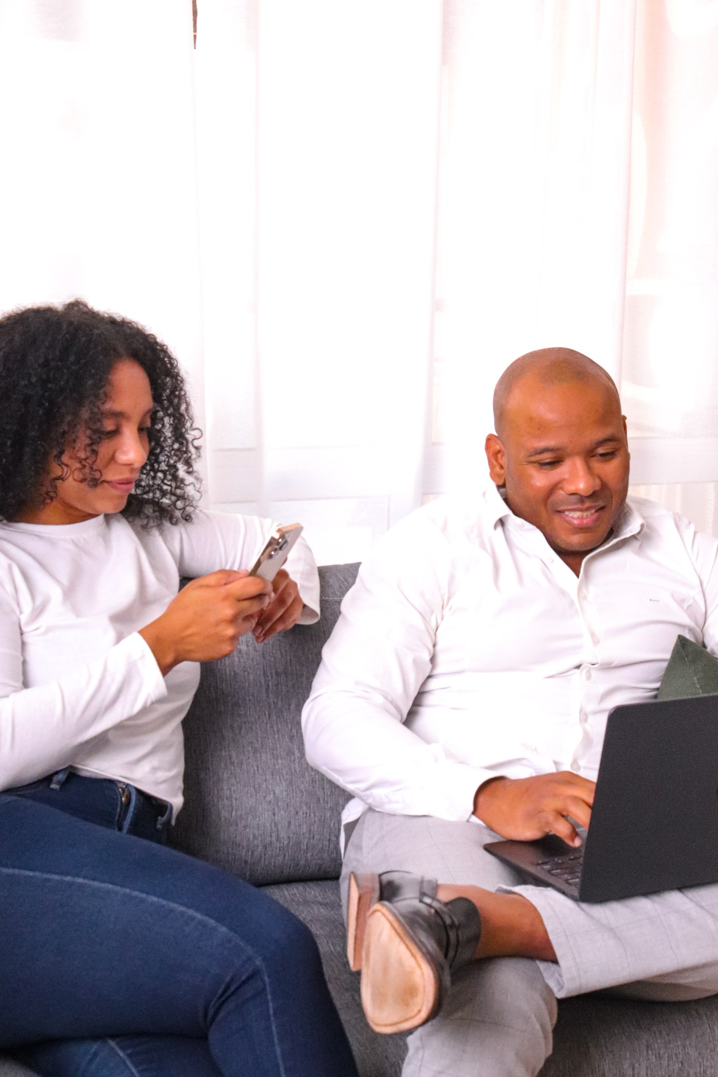 Os fundadores da Seguro Fácil sorrindo enquanto usam o celular e o notebook no sofá
